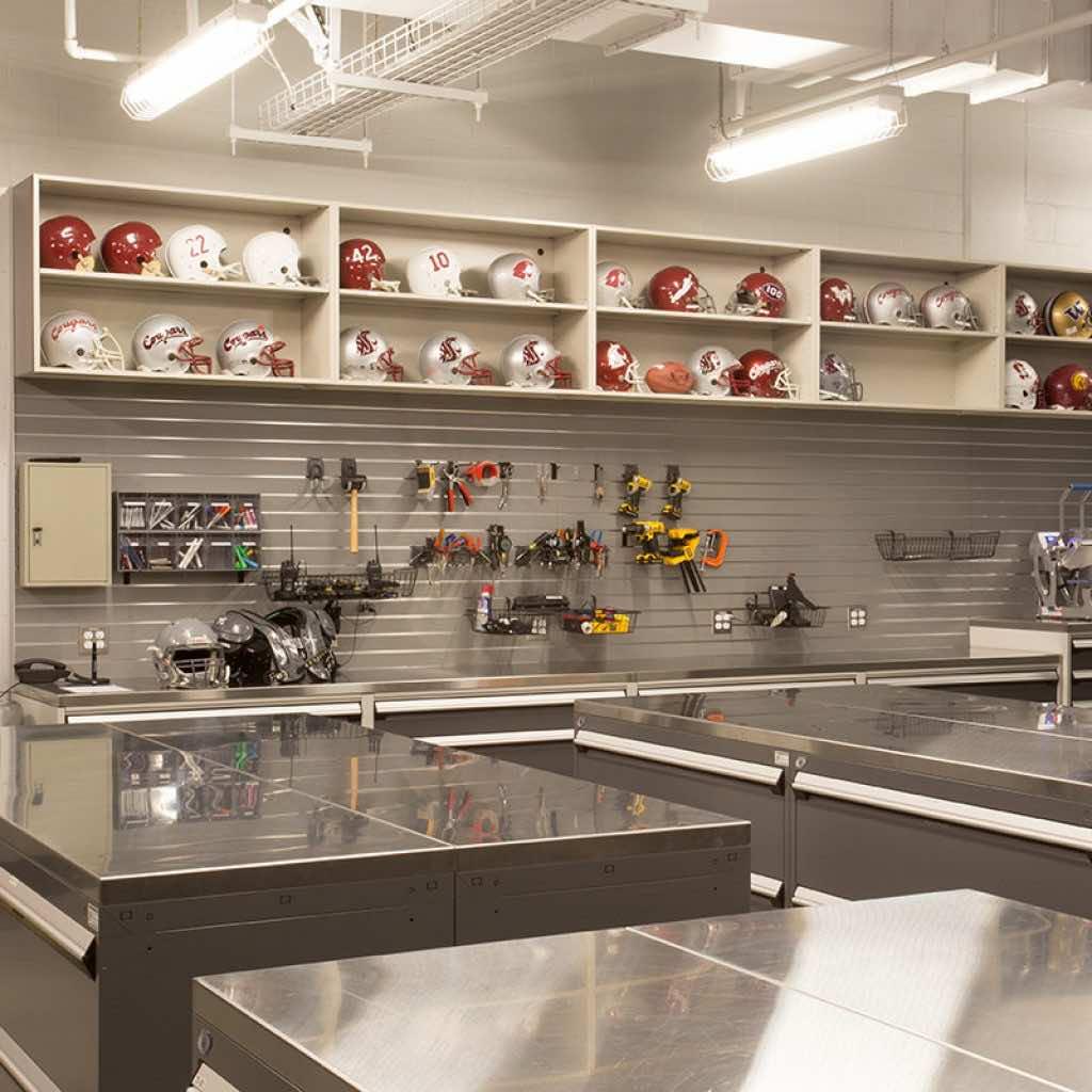 stainless steel countertops for gear repair in a football equipment room with shelves holding helmets in the background